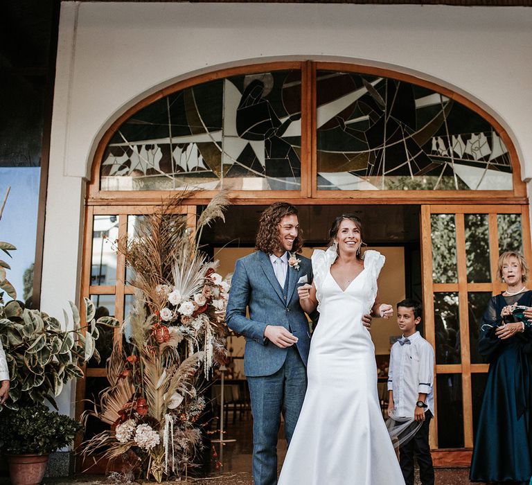 Bride and groom exit their wedding ceremony in a navy suit and ruffle sleeve wedding dress