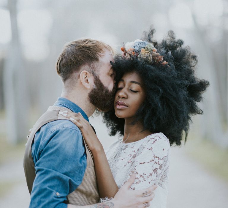 Bride with big afro embraces with groom. She wears a flower crown in her hair and lace wedding dress.