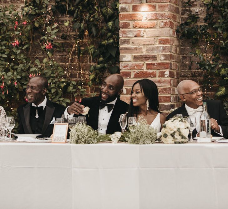 Black bride and groom sitting at the top table decorated with white and green flowers with their parents 