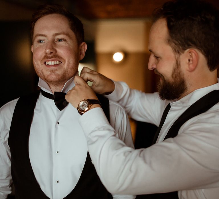 Groomsman fixing the grooms bow tie 