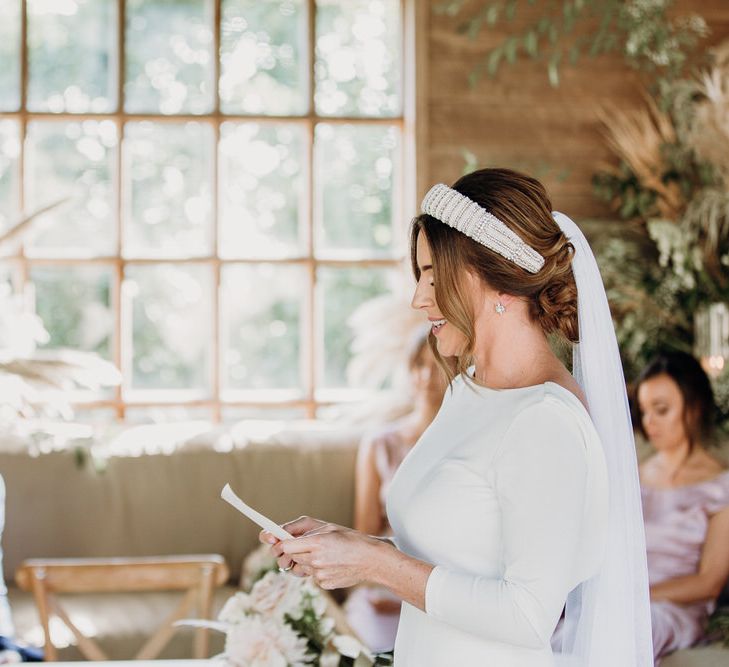 Emotional groom in navy suit looks at bride in Elbeth Gillis gown whilst she reads her vows at Euridge Manor wedding