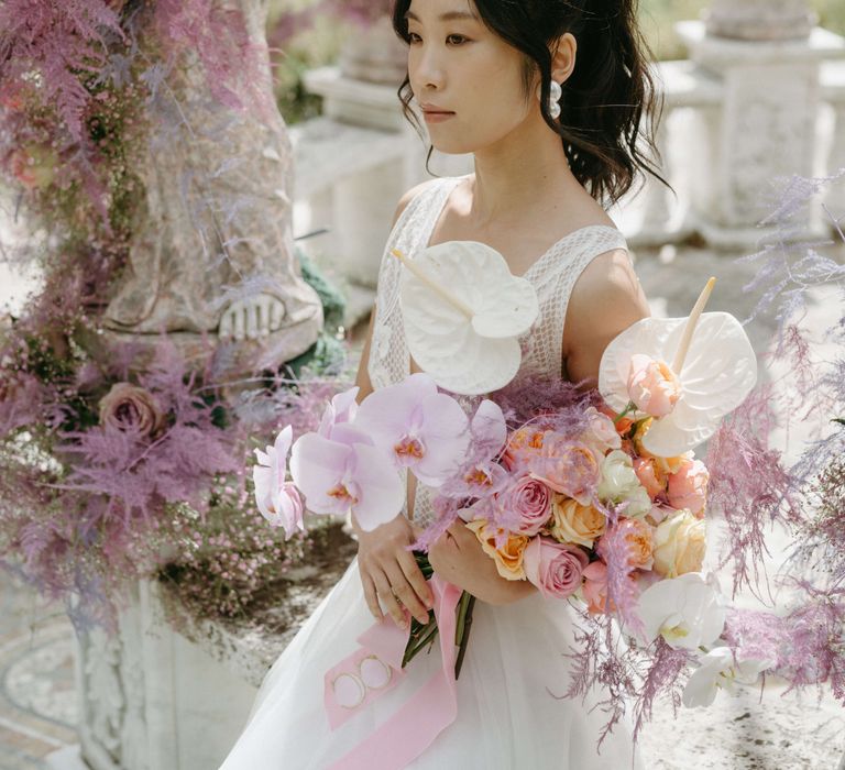 Bride looks ahead surrounded by lilac florals and holds pastel coloured bouquets