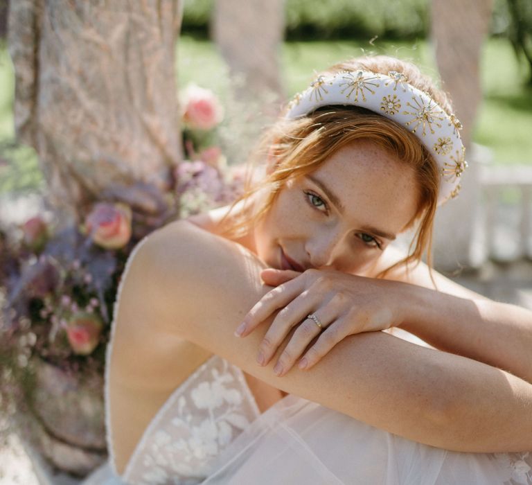 Bride looks toward camera wearing white headband and has arms folded