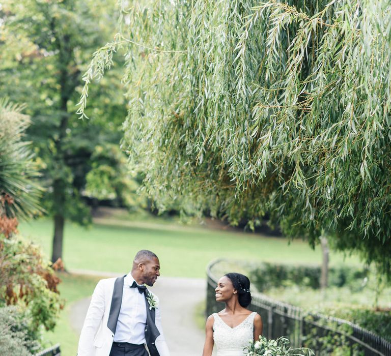 Bride & groom walk hand in hand outdoors surrounded by greenery