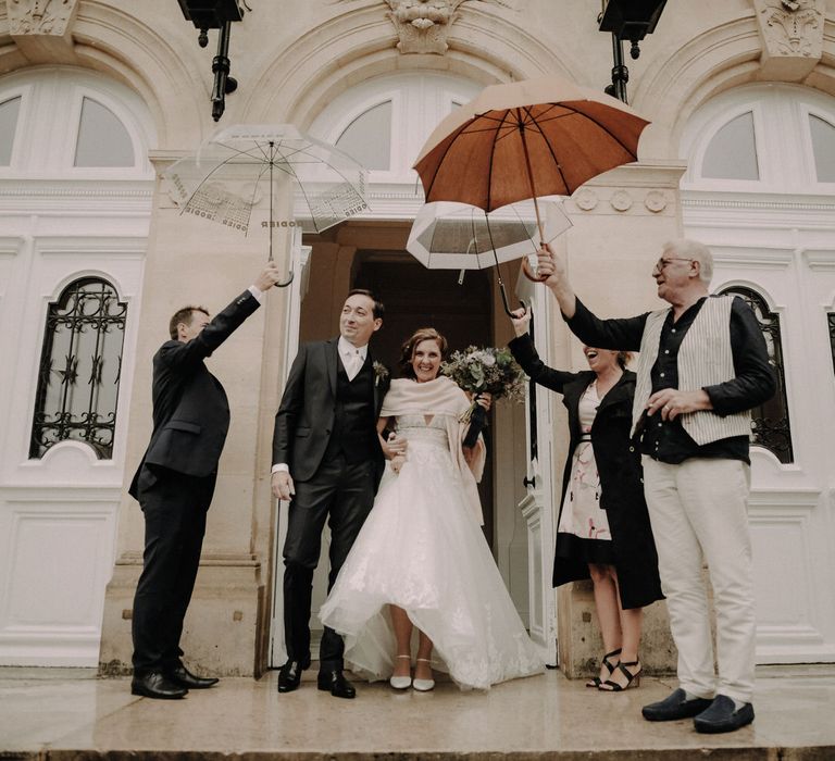 The bride and groom arm in arm leaving their ceremony as guests hold umbrellas over them