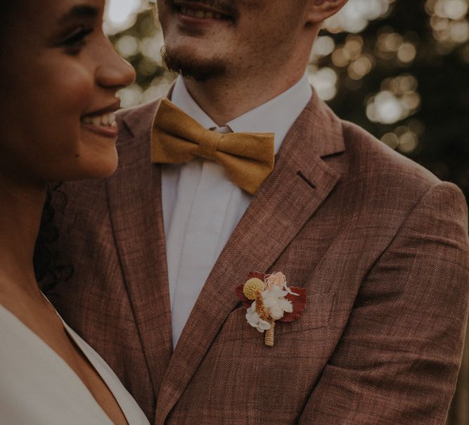 Groom in a brown check wedding suit and orange bow tie with a delicate buttonhole flower