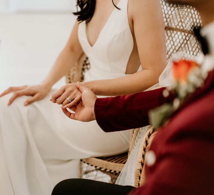 Groom holding his brides hand as they sit at their sweetheart table looking at her diamond engagement ring and wedding band 