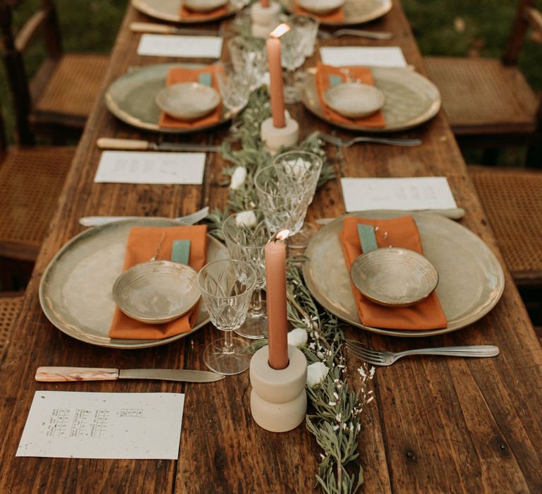 nature wedding reception table decor with green and orange tableware and linen, taper candles and greenery table runner 