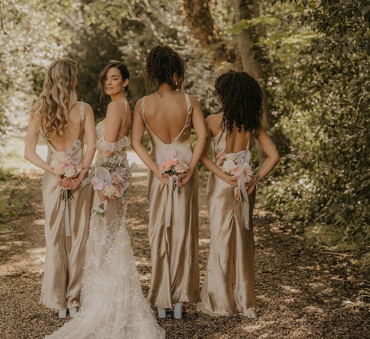 Bridal party in low back lace and satin dresses holding their pastel bouquets behind their backs 