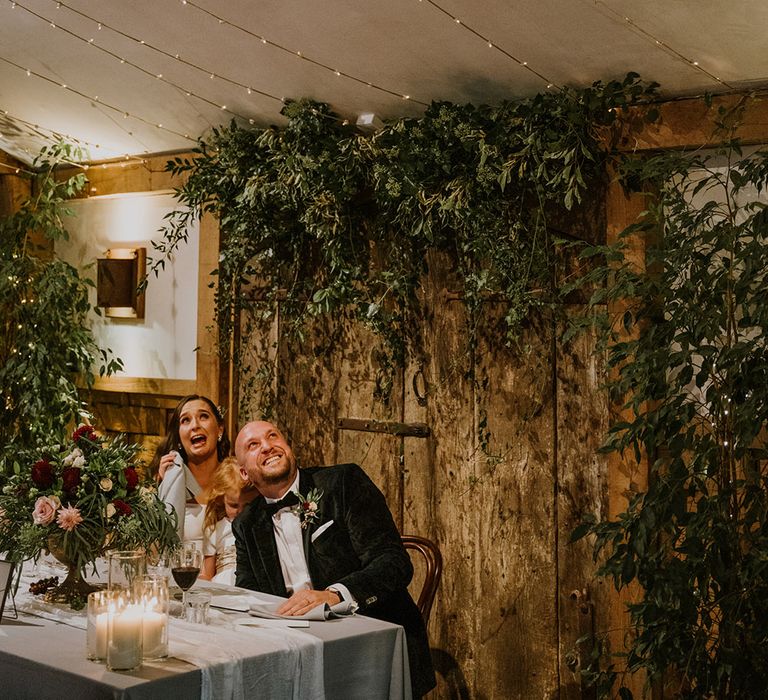 Bride and groom laughing during the wedding speeches with natural wedding decor 