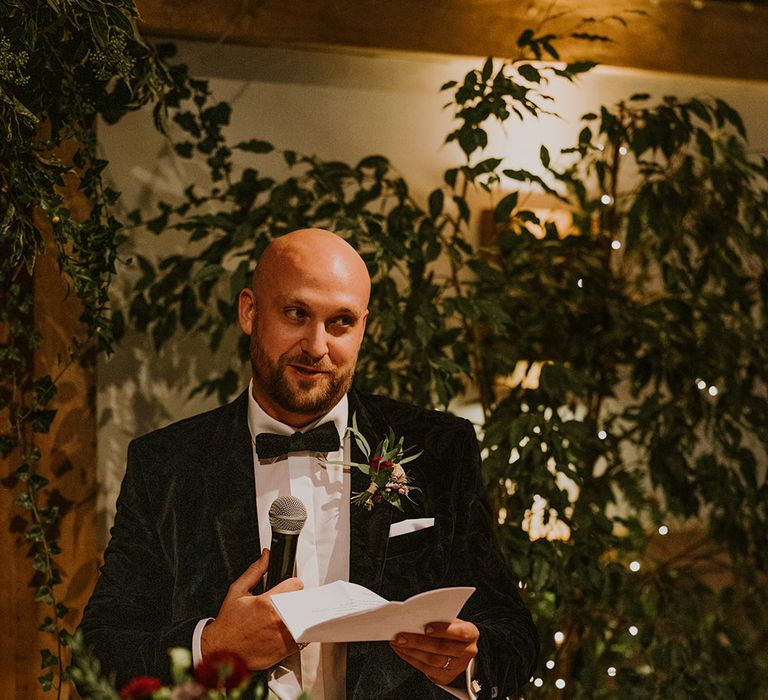 Groom in a velvet tuxedo jacket and bow tie delivering his wedding speech 