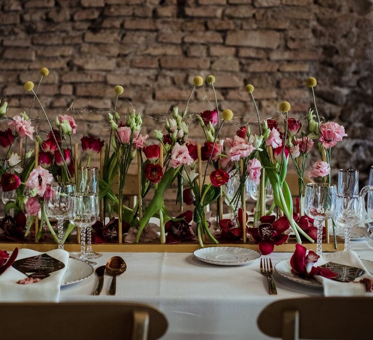 Floral table centrepiece with pink and red tulips, orchids, carnations and yellow craspedia