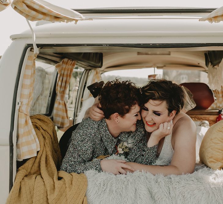 A lesbian couple lie looking out of a camper van window and laugh together. Photography by Caroline Goosey.