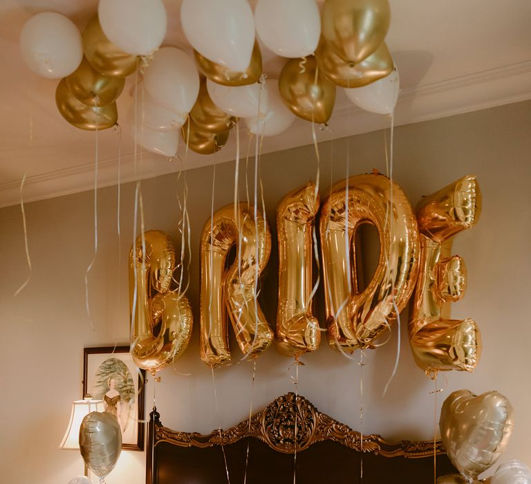 Large golden bride balloon above bed surrounded by heart shaped and round gold & white balloons