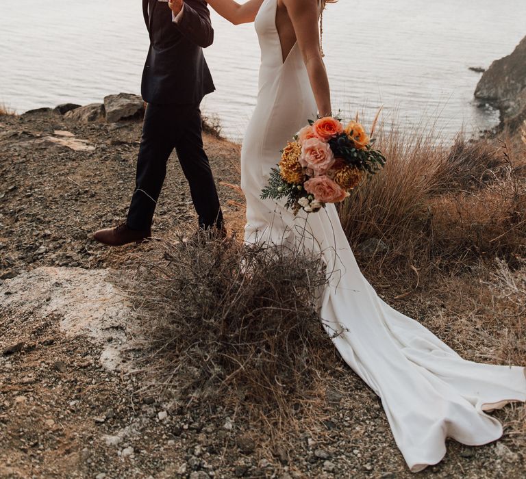 Groom leads bride along the cliffside during golden hour