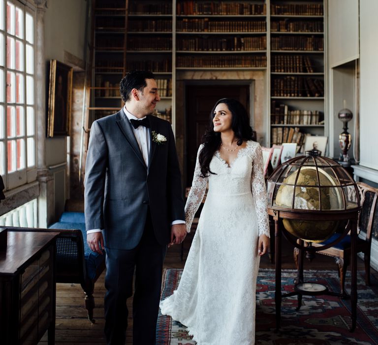 Bride & groom look lovingly at one another in front of bookcase 