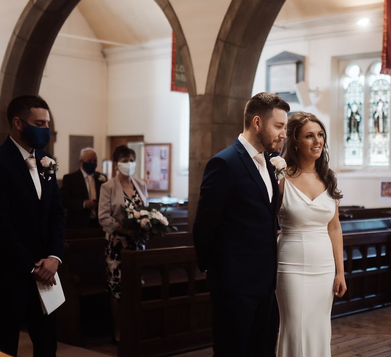 Bride and groom at the church altar, the bride is wearing a white slip wedding dress and the groom is wearing a navy suit