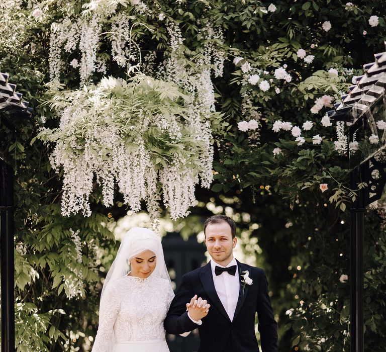 Bride and groom holding hands under hanging wisteria