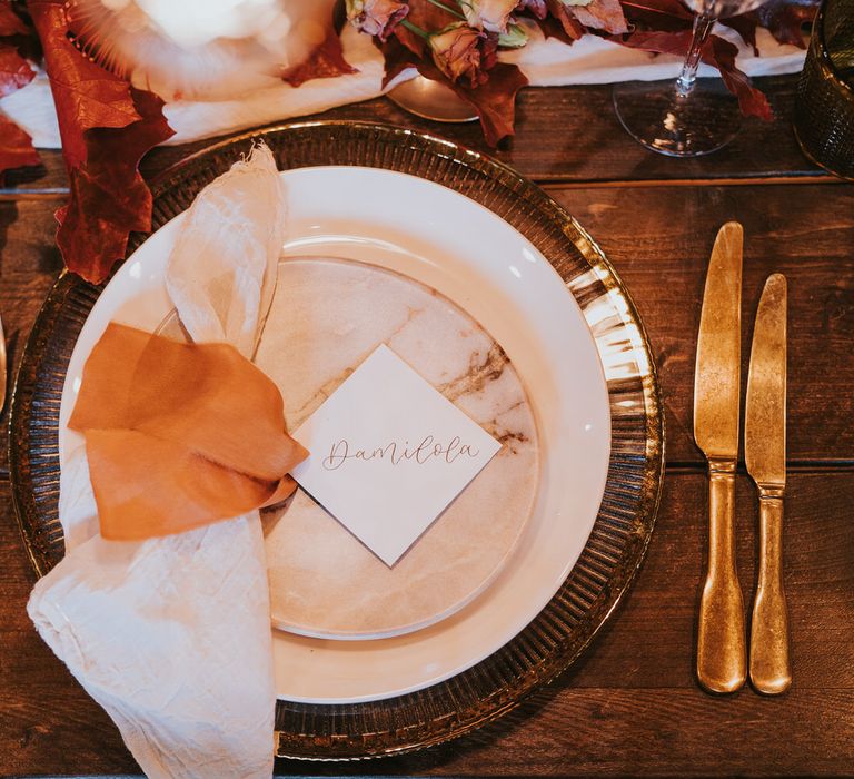 Gold, rust toned and orange place setting with marble side plate detail, gold cutlery and linen napkin