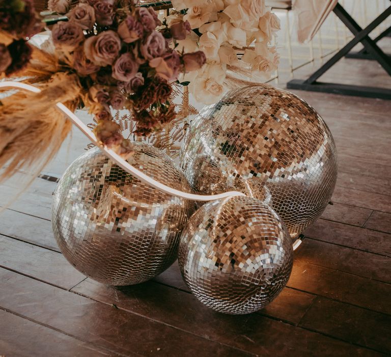 Three disco balls lay on wooden floor as florals hang from the table