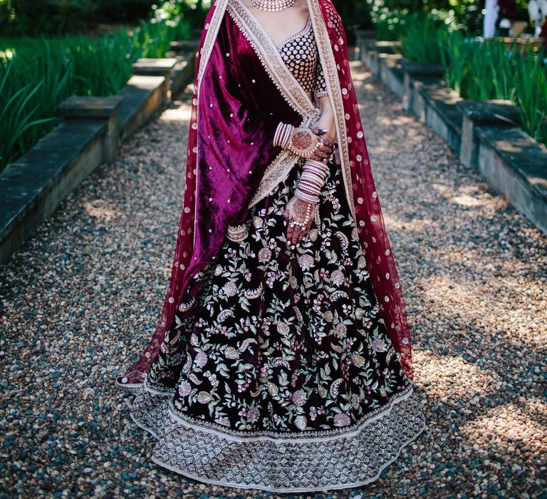 Bride wears beautiful deep red and pink lehenga on her wedding day whilst stood outdoors