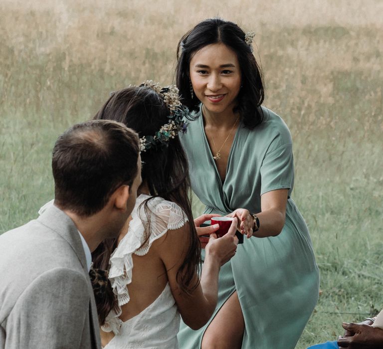 Bride & groom during Chinese Tea Ceremony as bridesmaid holds out tea whilst wearing sage green bridesmaids dress