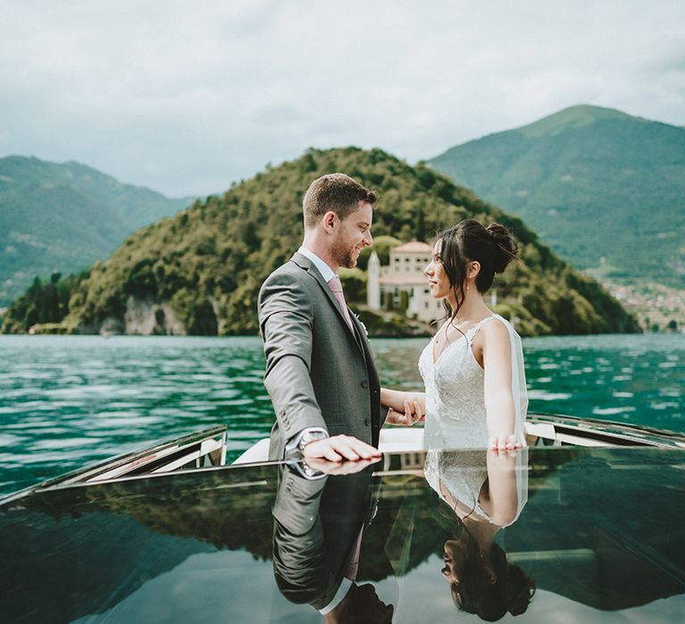 Bride & groom look lovingly at one another as they stand on boat on Lake Como 