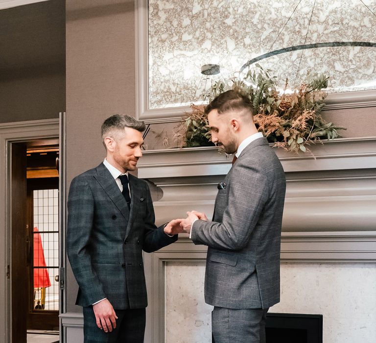 Groom puts on wedding ring for husband on their wedding day during ceremony within the Old Marylebone Town Hall