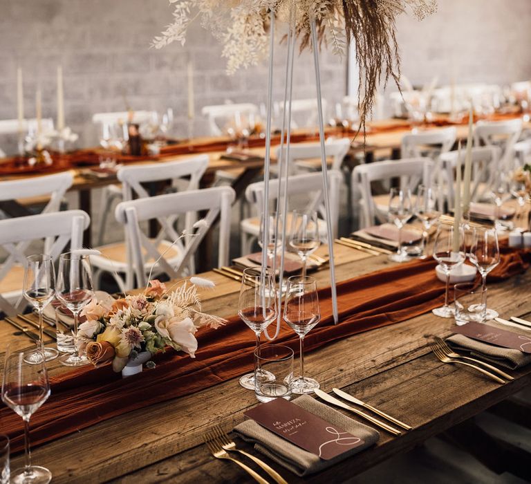 Boho wedding breakfast with long wooden table, burgundy table runner, pampas grass, white chairs and white drapery for summer wedding in Dorset