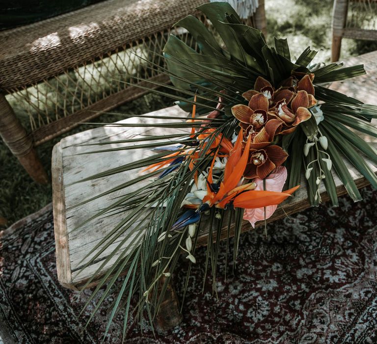 Tropical bridal bouquet resting on low wooden table for birds of paradise wedding inspiration