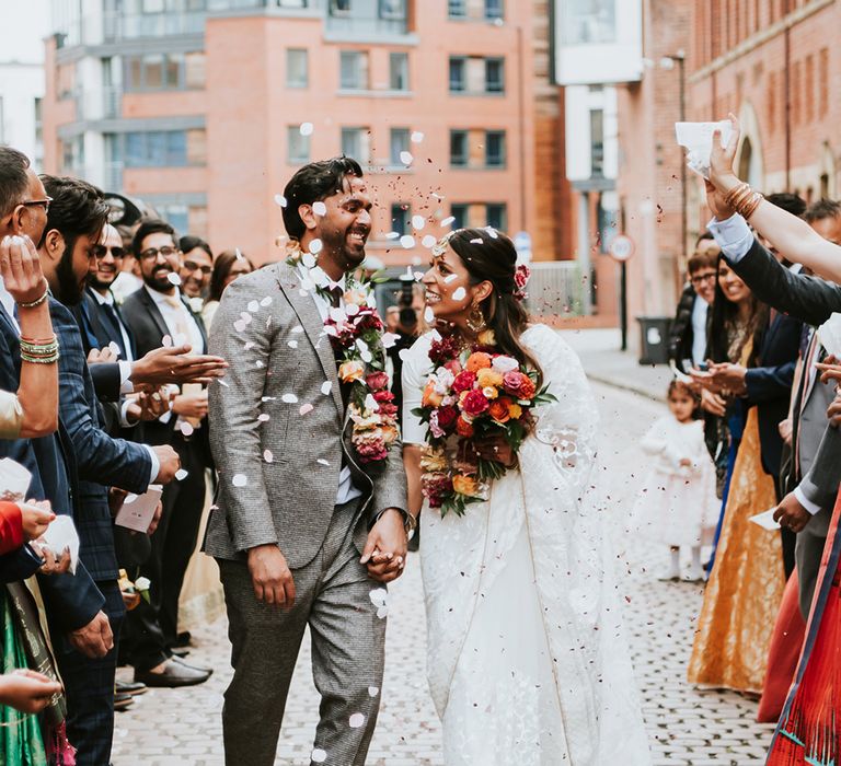 Indian British wedding with the bride and groom walking through a confetti shower.