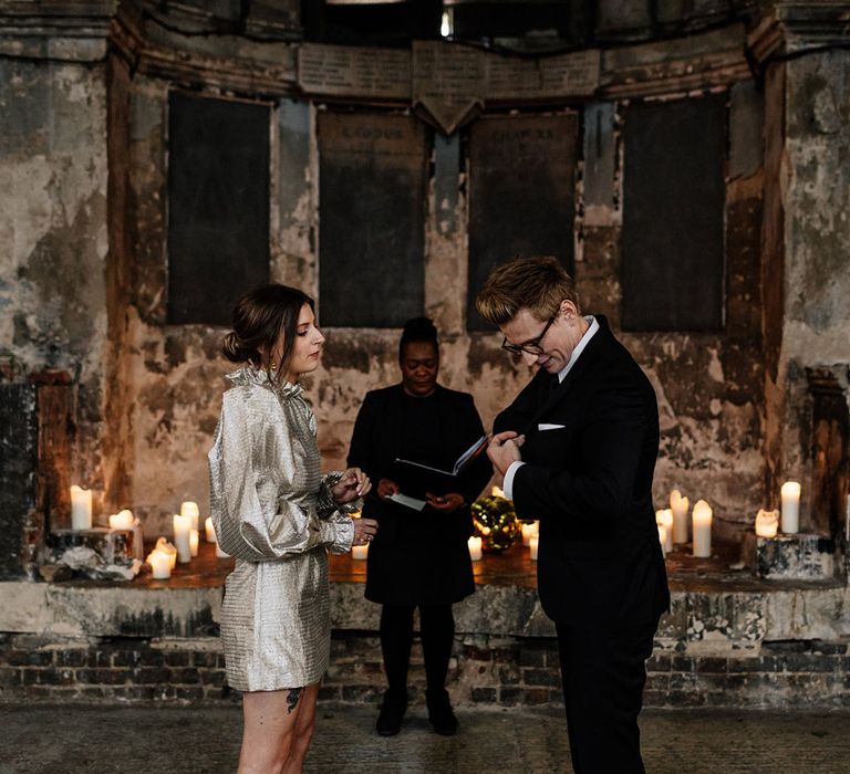 Groom stands in black fitted suit in front of Bride in funky gorgeous short gold wedding dress 