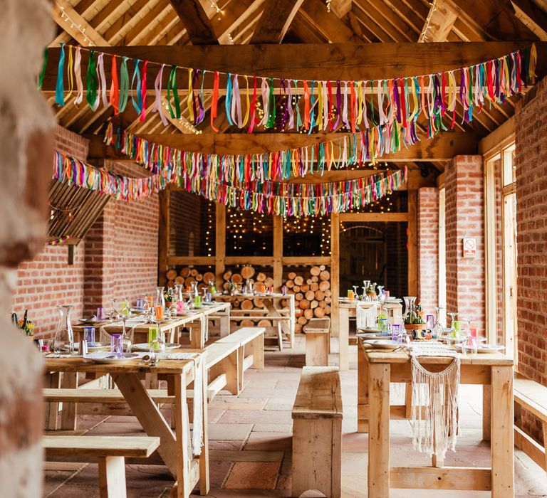 Interior of The Bridal Barn wedding venue for rustic wedding breakfast with colourful streamers, colourful glassware and wooden tables and benches