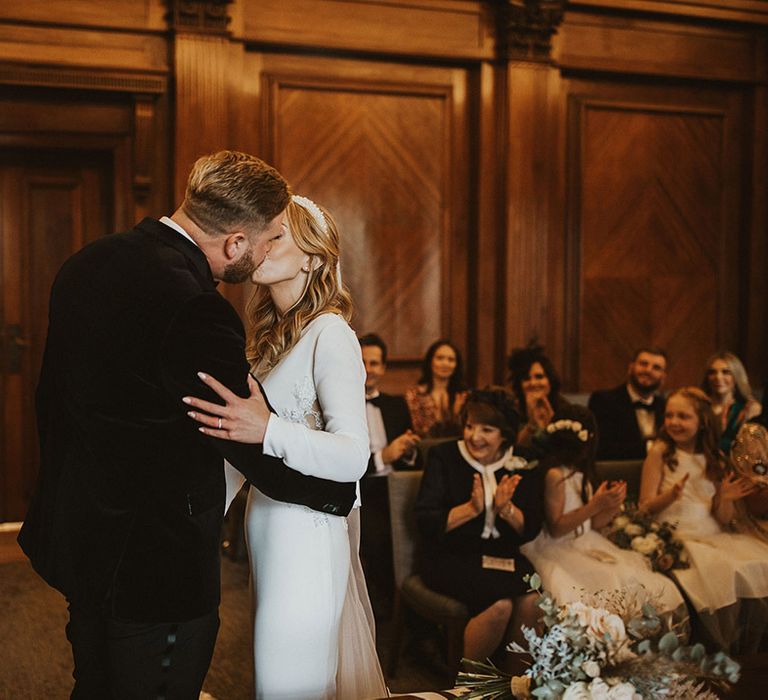 Bride in a long sleeve wedding dress kissing her husband in a tuxedo at their registry office wedding 