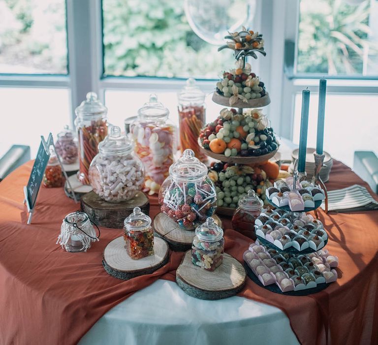 Dessert table complete with balloon archway and orange tablecloth in front of window 