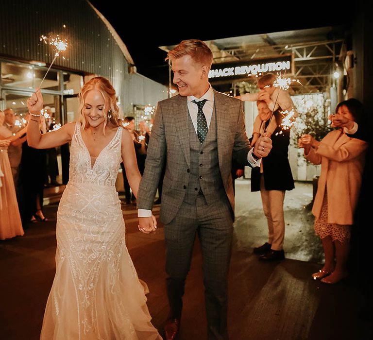 Bride in Eleganzza Sposa wedding dress with groom in check suit during sparkler exit