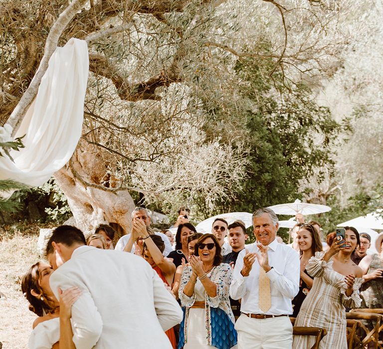 Wedding guests applaud as bride and groom share their first kiss as a married couple