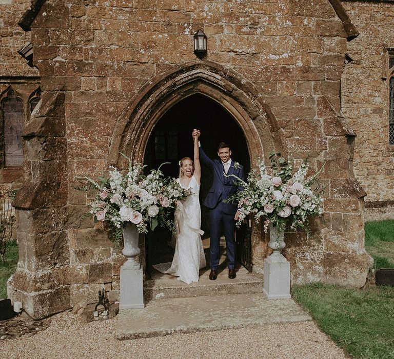 Bride and groom exit the church decorated with pillars of pink, white and green flower display