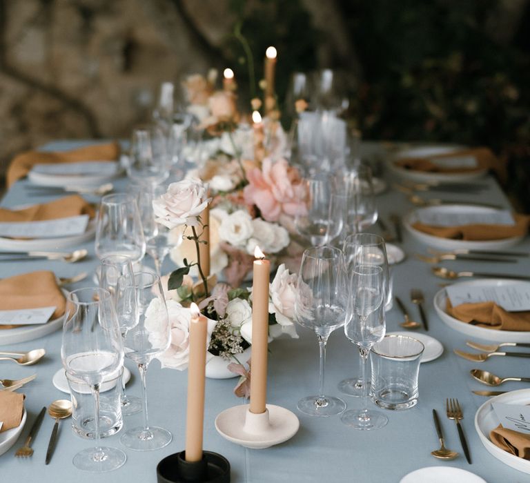 Pastel themed table setting with grey tablecloth and peach candles and napkins with white and pink flowers 