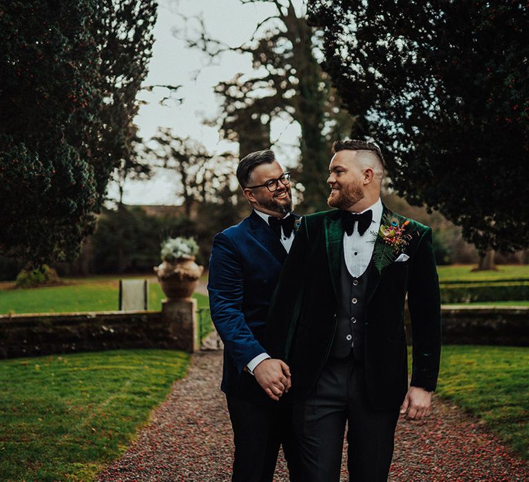 Grooms in blue and green velvet suit jackets with matching black bow ties for the LGBTQI+ wedding 