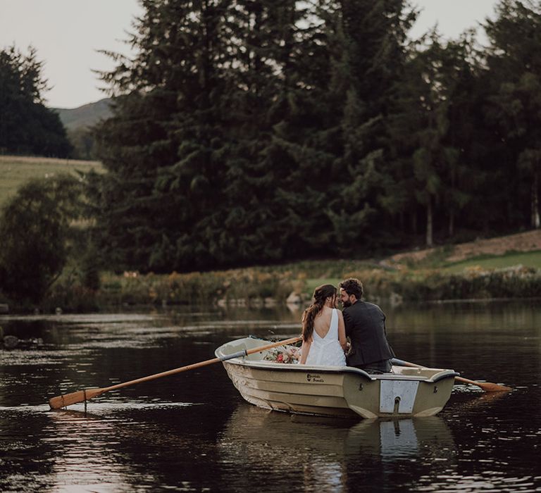 Bride and groom in a row boat on loch at Cardney Estate wedding venue with Socttish hills in the background and horses 