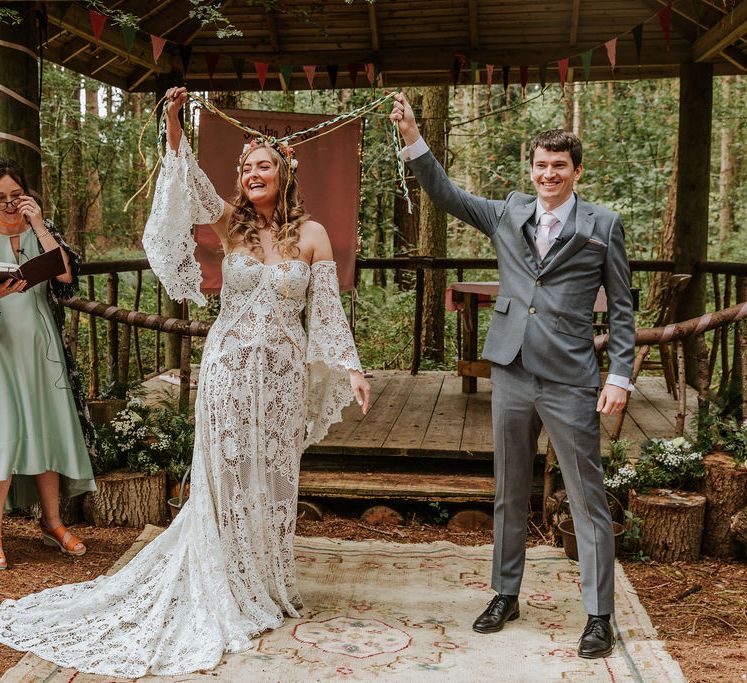 Woodland wedding ceremony with bride in a medieval wedding dress holding her hand fasting rope in the air after the ceremony 