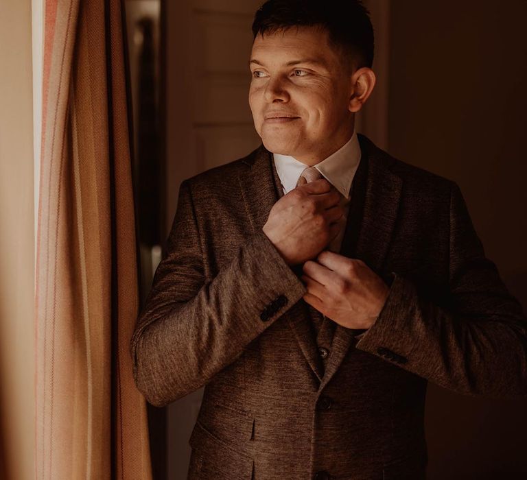 Groom fixes his tie as he gets ready for his wedding day at Eden Barn