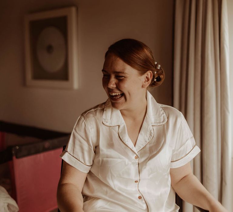 Bride wears silk pyjamas on the morning of her wedding day with her hair in Chignon bun complete with pearl hair accessories 