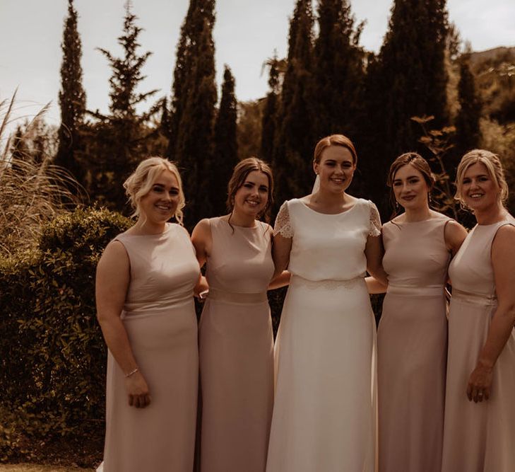 Bride stands with her bridesmaids who wear pale pink dresses complete with capped sleeves 