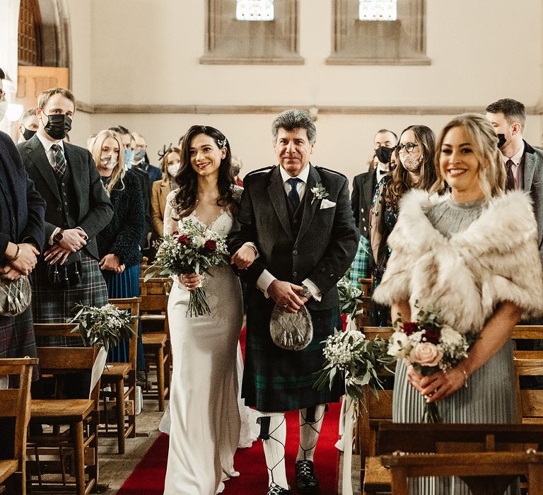 Bride walks down the aisle holding red and white floral bouquet for winter wedding in Scotland 