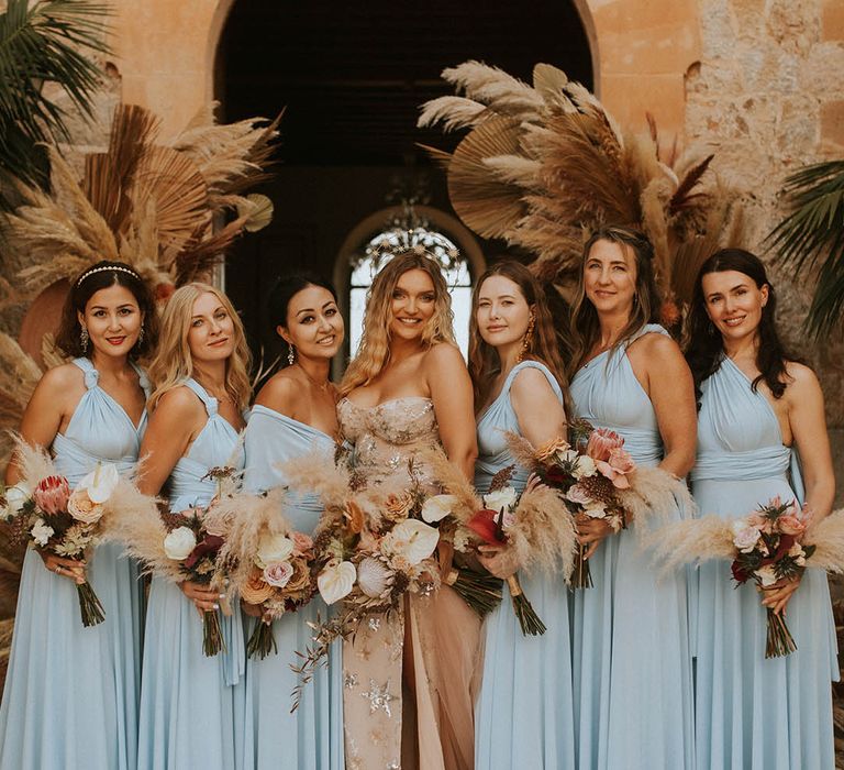 Bride in celestial wedding Dres with bridesmaids in pale blue dresses with pampas grass bouquets with warm toned flowers