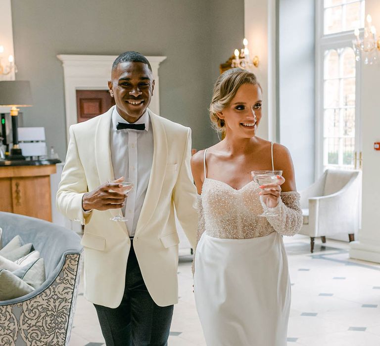 Bride in beaded off the shoulder second wedding dress with the groom wearing a white suit jacket and black trousers for the evening 