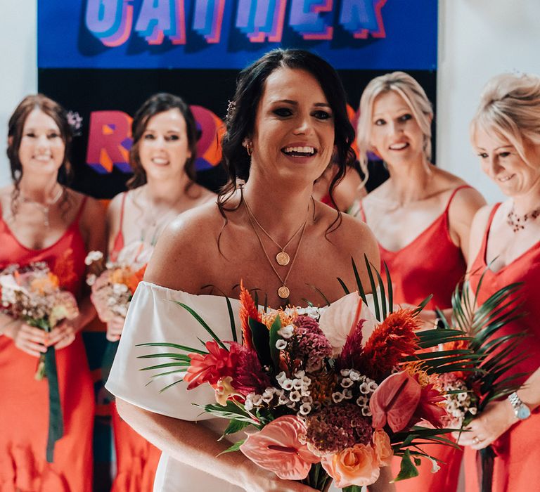 Bride holding a pink and orange vibrant tropical wedding bouquet with palm leaves 