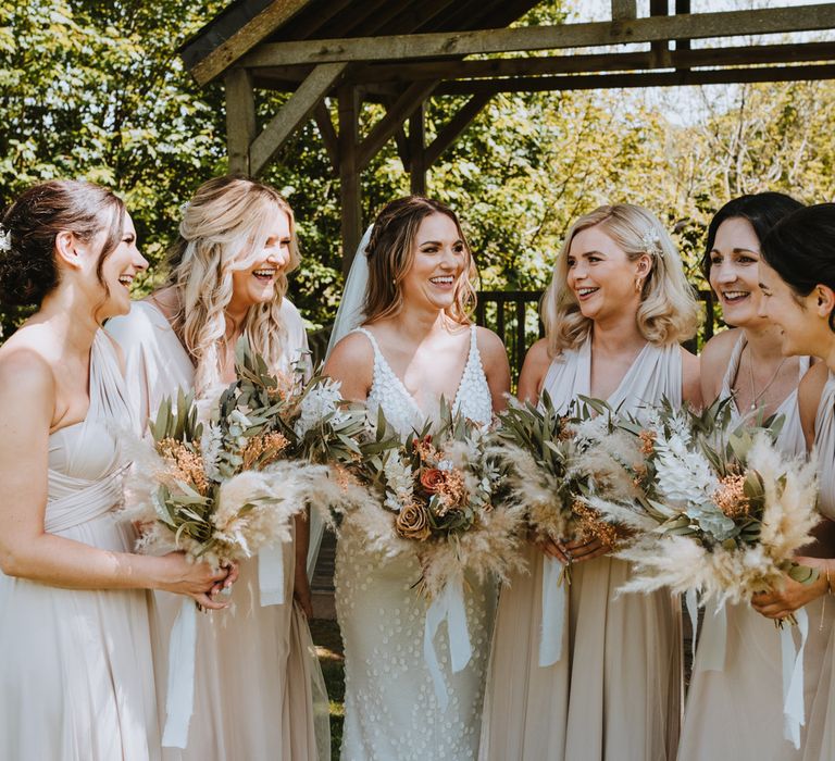 Bridal party wearing light cream bridesmaid dresses and bride wearing sleeveless Made With Love Bridal dress all holding dried flower bouquets with burnt orange and toffee coloured roses